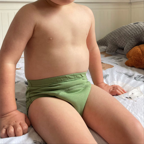 Young child wearing a Brolly Snazzi Pants Day Trainers green diaper sitting on a bed - Sprout