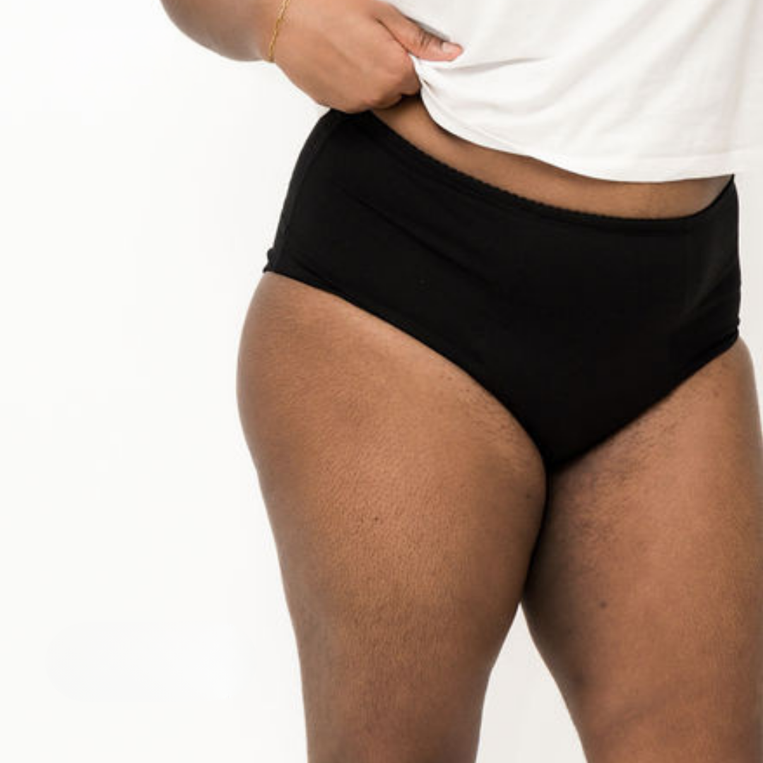 A lady wearing black high-waisted absorbent underwear and a white t-shirt on a plain background